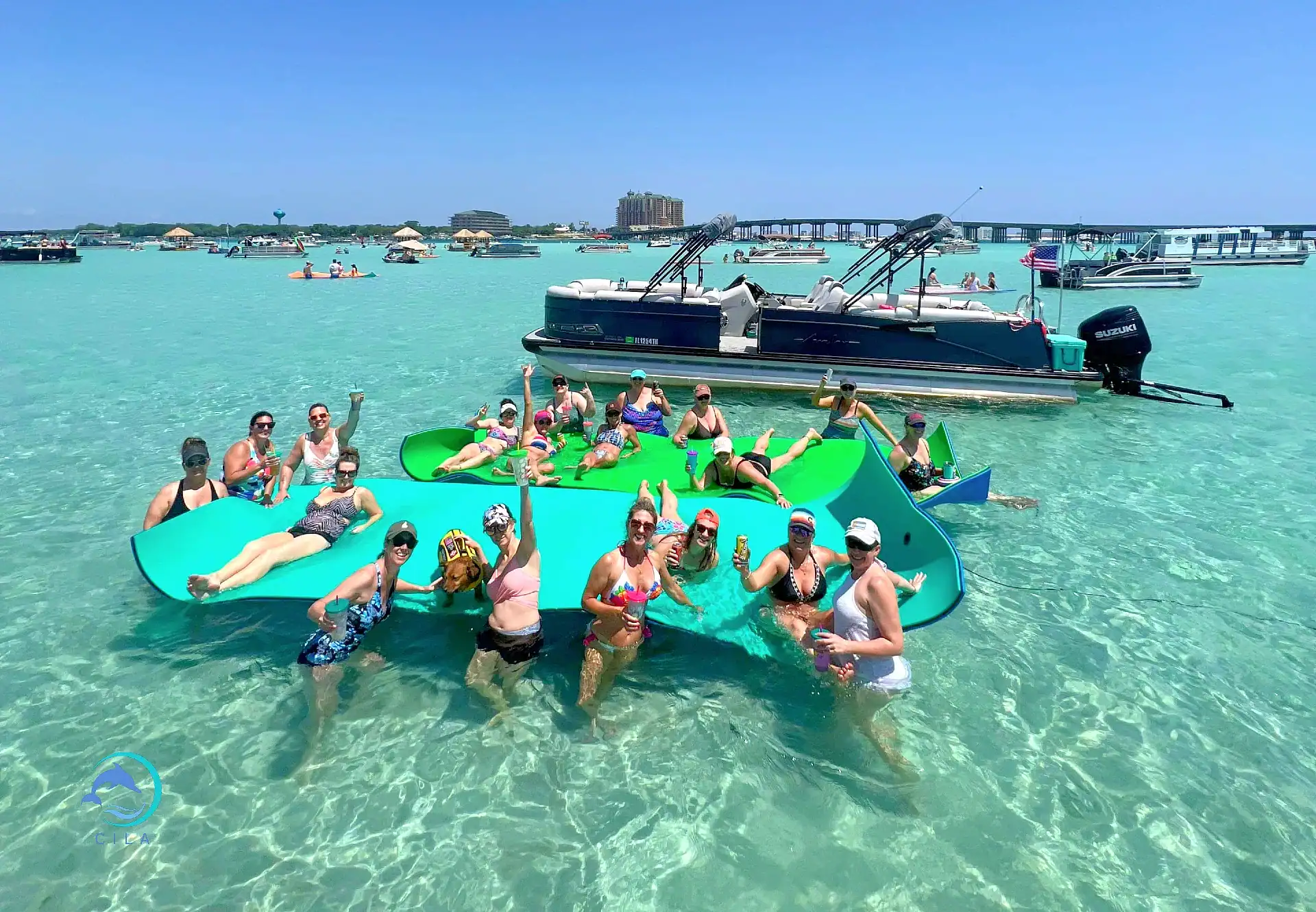 Vibrant group of friends enjoying Crab Island's clear waters on floating mats, with boats and blue skies in the background.
