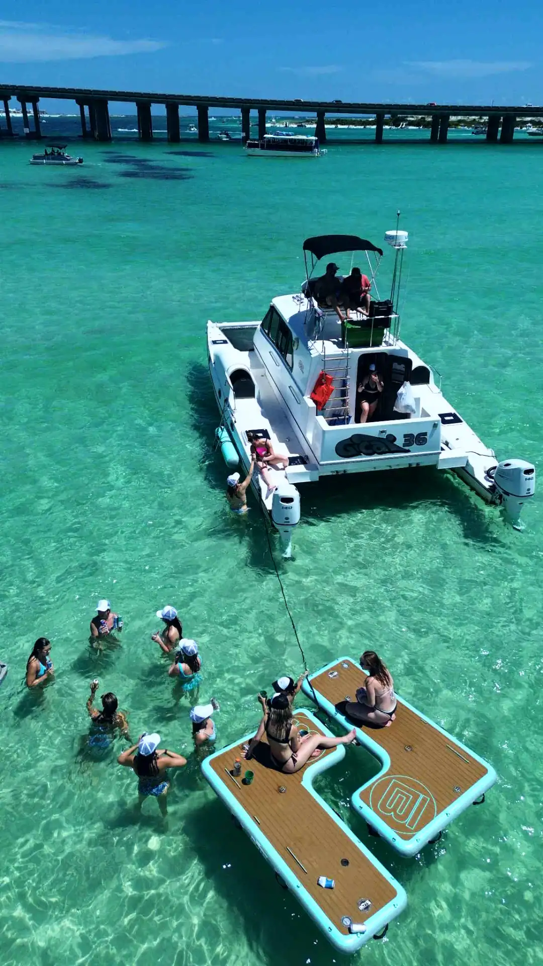 Luxury Catamaran anchored at Crab Island with Bachelorettes floating in emerald green water nearby.