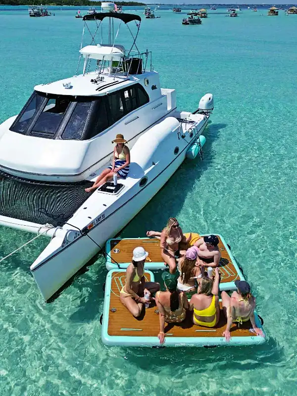 Group of friends hanging out on BOTE floats at Crab Island near a white catamaran