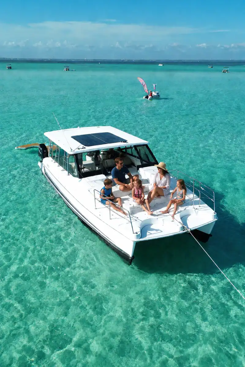 Family sitting on the deck of a white catamaran anchored at Crab Island surrounded by crystal clear emerald water.