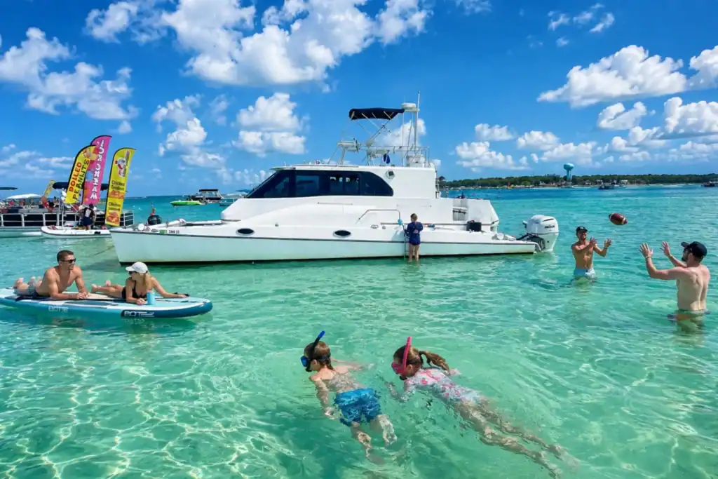 Lady Delana, white catamaran, anchored at Crab Island with people enjoying snorkeling, BOTE floats, and football.